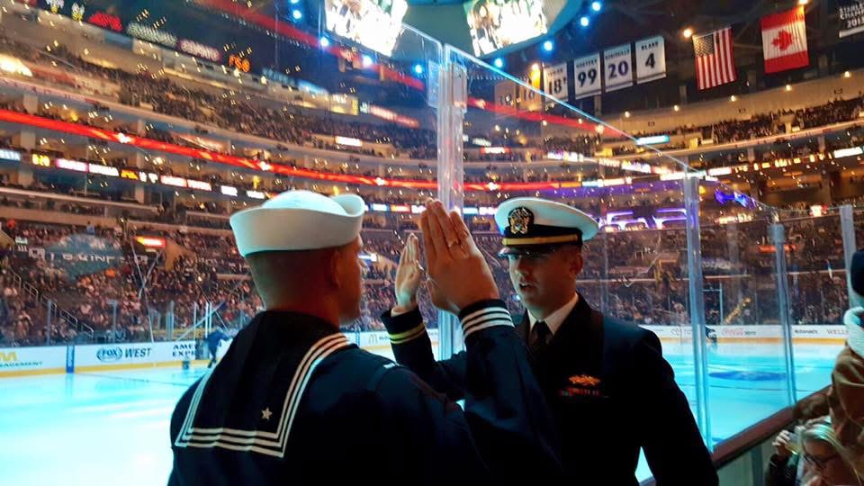 An image of two individuals wearing U.S. Navy Uniforms, standing in an arena or stadium